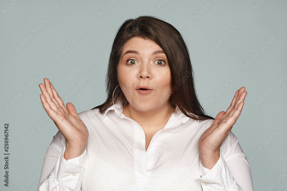 Isolated shot of emotional bug eyed plus size young lady wearing formal white shirt, expressing astonishment, exclaiming excitedly, gesturing surprisingly, her eyes full of disbelief and amazement Isolated shot of emotional bug eyed plus size young lady wearing formal white shirt, expressing astonishment, exclaiming excitedly, gesturing surprisingly, her eyes full of disbelief and amazement