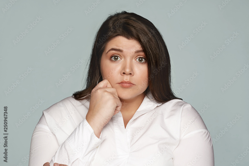 Human facial expressions, emotions, reaction and feelings. Attractive scared young chubby dark haired female employee in formal wear having worried nervous fearful look, opening eyes widely Human facial expressions, emotions, reaction and feelings. Attractive scared young chubby dark haired female employee in formal wear having worried nervous fearful look, opening eyes widely