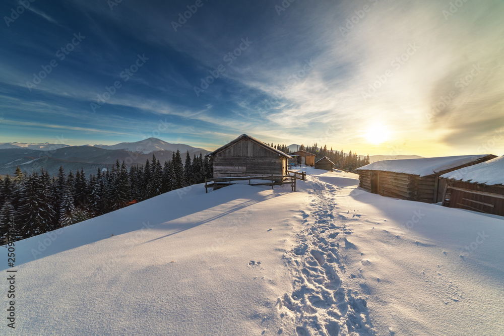 A colorful evening with a beautiful sunset and dusk in the snow-covered mountains of the mountains with mountain houses in the Ukrainian Carpathians overlooking Hoverla and Petros.