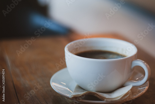 Coffee mug filled with americano coffee on the plate with brown tissue paper on vintage wooden table