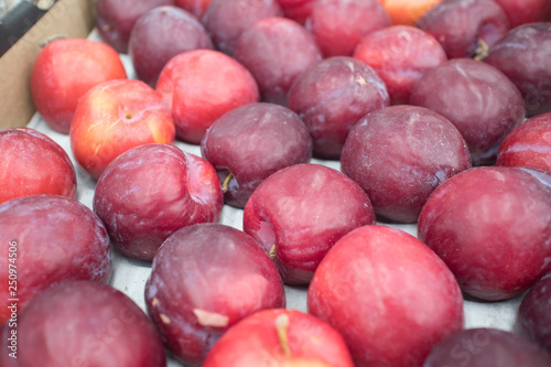 Texture of red plum in shop close up top view. Box with plums in store. Tasty sweet fruit for dessert, salad, juice.