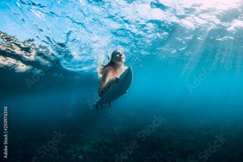 Surfer girl with surfboard dive underwater