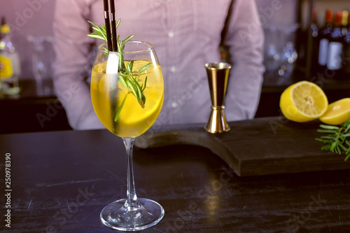 Alcohol cocktail with sparkling wine, ice and liquor , lemon and rosemary in wineglass on bar counter, close-up view.