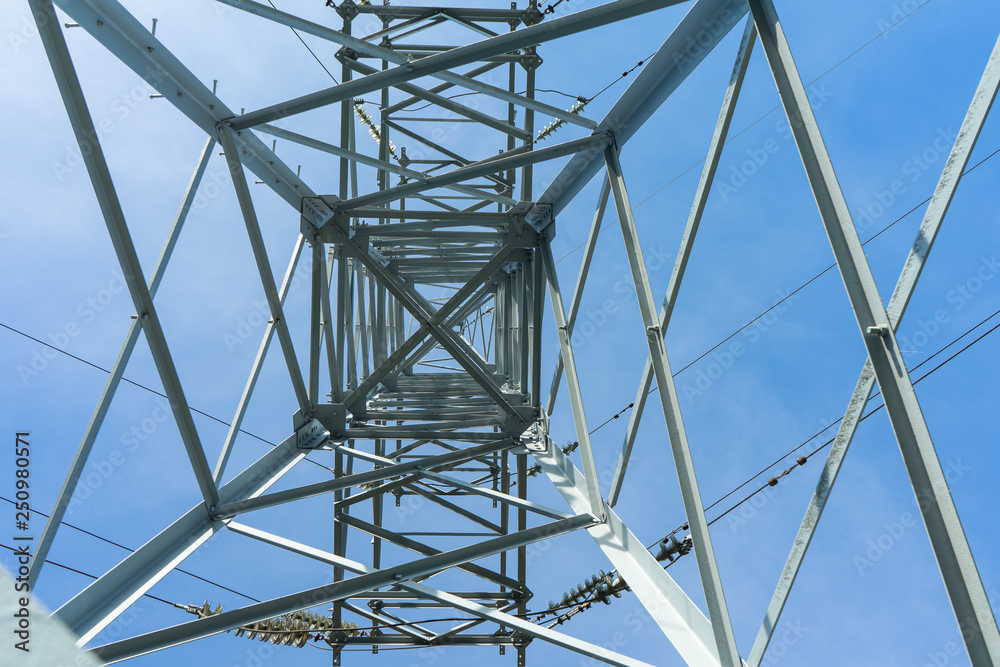 Supports high-voltage power lines against the blue sky with clouds. Electrical industry.