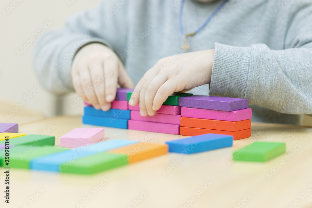 Child playing with building blocks learning new skills.a hand is putting last cube on the top of pyramide Child playing with building blocks learning new skills.a hand is putting last cube on the top of pyramide