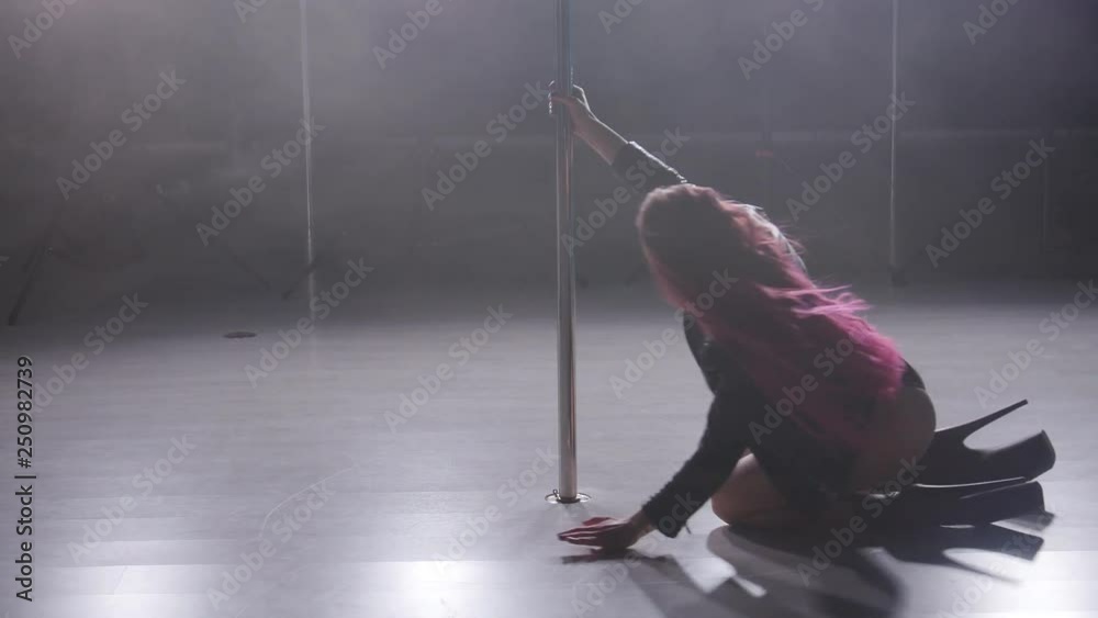 Concept of dance and acrobatics. Young slim woman pole dancing in dark interior with backlight and smoke