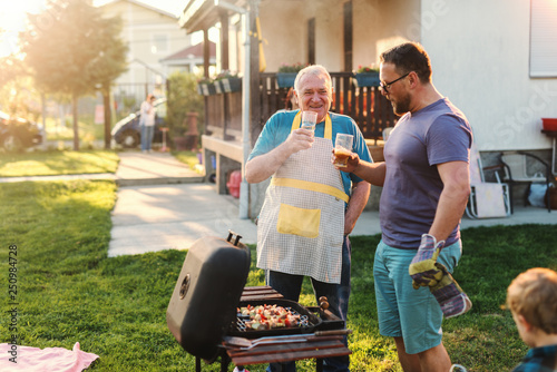 Photography Cheerful father and son drinking beer while standing next to grill in backyard at summer