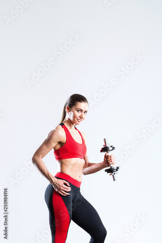 Fit woman with dumbbells in sportswear red-black on a gray background.