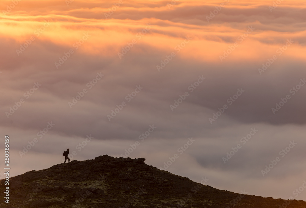 Silhouette of a man on the ridge above the sea of clouds, misty mountains at sunset in Iceland Silhouette of a man on the ridge above the sea of clouds, misty mountains at sunset in Iceland