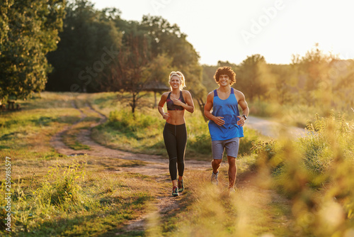 Happy Caucasian couple in sportswear with healthy habits running in nature. Sunny summer day.