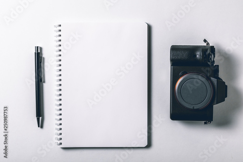 Modern white office desk table with pen and digital camera mirrorless. Blank notebook page for input the text in the middle. Top view  flat lay.