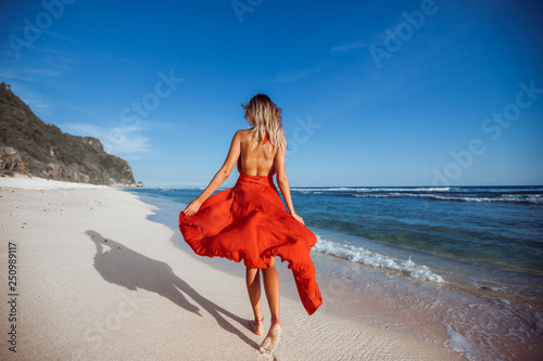 фотографія Girl walking on the beach in red dress back view