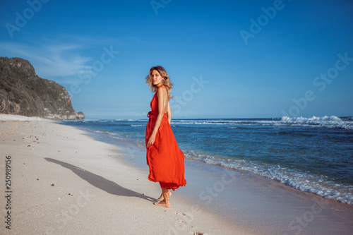 Girl walking on the beach with white sand in a red dress