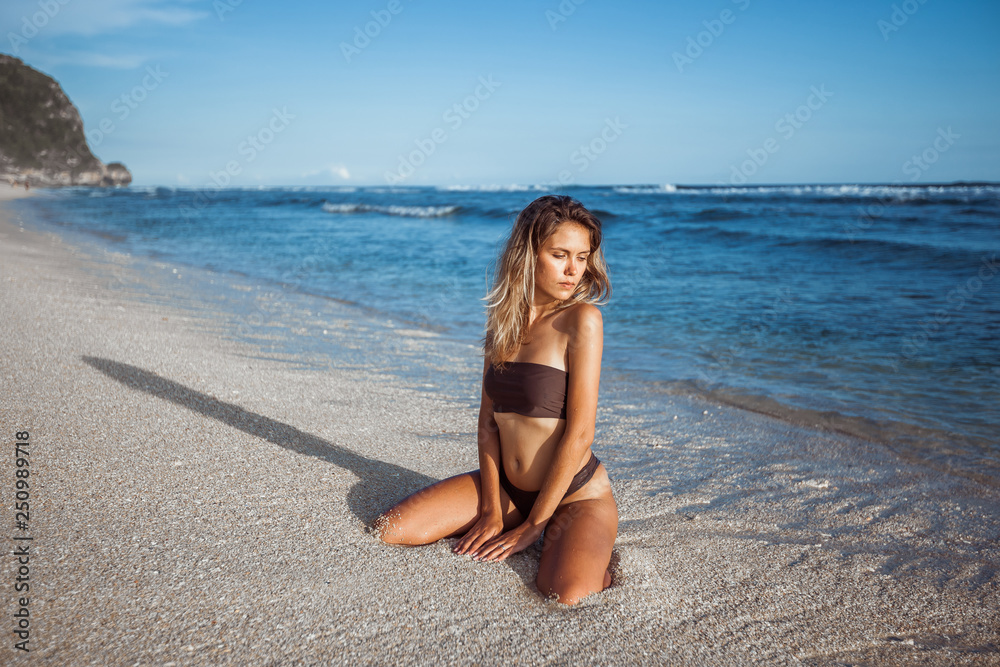 Sexy girl in swimsuit sitting on her knees on the beach.