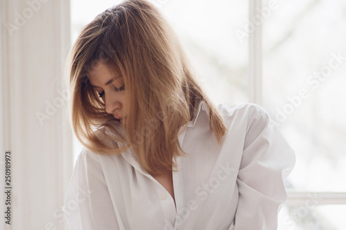 Portrait of a young beautiful woman at the window. Girl in white shirt © Ulia Koltyrina