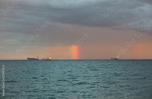 Short rainbow over sea, between three big tankers, under heavy clouds © Wioletta