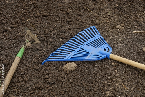 two garden tools made of iron sap and blue platypace rake lie on gray ground