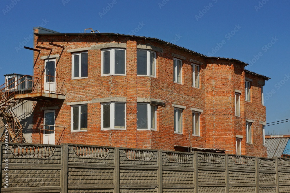 large brick brown house with windows behind a gray concrete fence