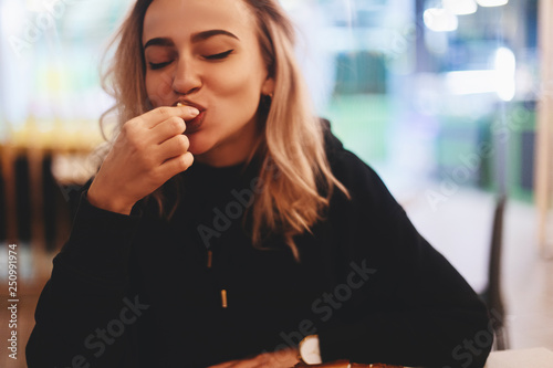 Funny blonde woman in black hoodie eating cheese balls at restaurant.