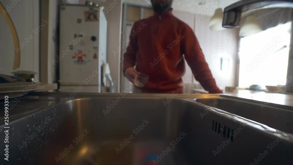 bearded lifestal man pours water from the tap into a glass and drinks