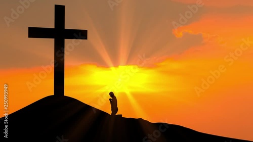 Silhouette of christian man praying to the cross on the hill at sunset time. Shot in 4k resolution photo