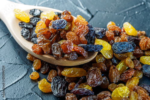 Assortment of Raisins, yellow, blue, black, golden raisin in wooden spoon scattered on dark table of kitchen. Healthy snack, dietary product for good life. copy space, Vega Food.