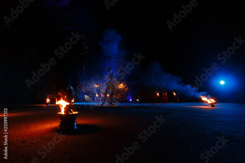 Fire show, dancing with flame, male master juggling with fireworks, performance outdoors, draws a fiery figure in the dark, bright sparks in the night.