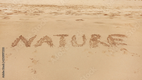 Word NATURE hand written in wet sand of beach.