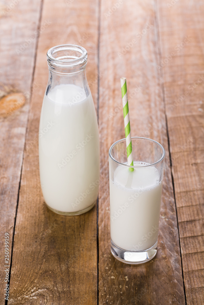 Bottle and glass of milk with straw on wooden table Bottle and glass of milk with straw on wooden table