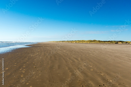 Beach tire tracks with ocean and dunes, deep blue sky without clouds