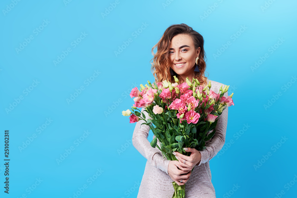 Young happy smiling redhead woman holding bouquet of colorful spring flowers isolated on blue background Young happy smiling redhead woman holding bouquet of colorful spring flowers isolated on blue background