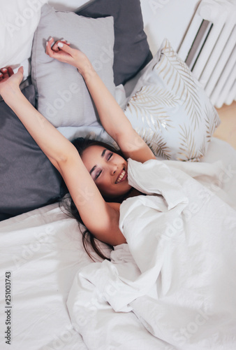 Happy smiling beautiful long hair asian girl young woman lying down in bed, cozy morning