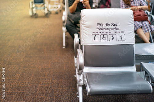 White and grey piority seat near gateway in the airport, with blur passengers behind. (Thai and Chinese language  means 