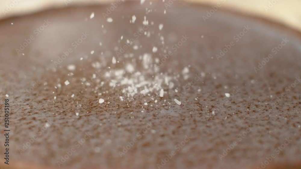 SLOW MOTION, DOF, CLOSE UP: Coarse crystals of rock salt are scattered across the granite countertop. Cinematic shot of white crystals of sugar bouncing off the hard gray stone surface of the table.