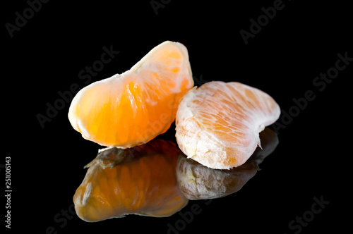 Tangerines or mandarins slices on black reflective background.