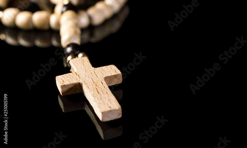 Wooden rosary beads with cross on black reflective background. Space for text.