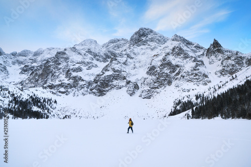 The traveler is walking on ice of the Lake of Morskie Oko in winter mountains