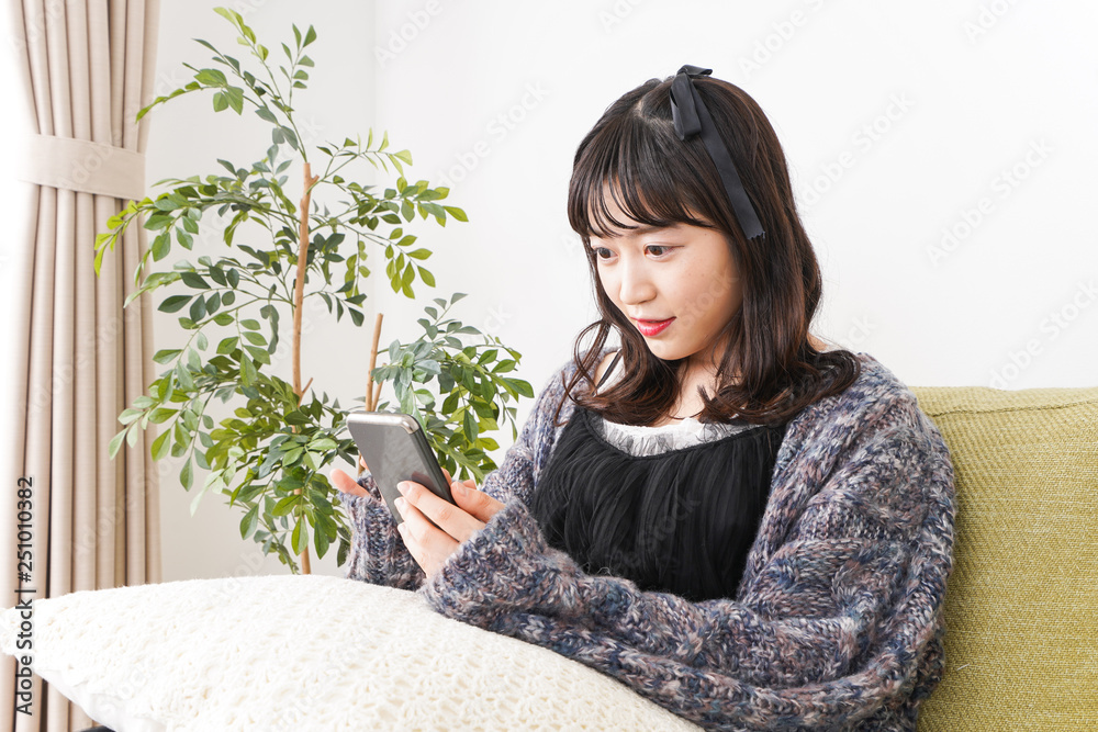 家でスマートフォンを使う若い女性 家でスマートフォンを使う若い女性