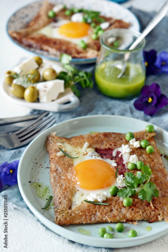 Breton traditional pancake made from buckwheat flour with ham, cheese, egg, feta, green peas and green butter. Breakfast of buckwheat thin pancakes with fried eggs, ham and cheese. Breton traditional pancake made from buckwheat flour with ham, cheese, egg, feta, green peas and green butter. Breakfast of buckwheat thin pancakes with fried eggs, ham and cheese.
