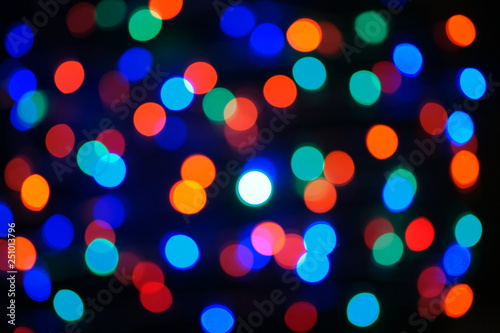 Multi-color blue holiday garland. Garland is blurred. Many big colorful round lights. Fully defocused photo. Blurred background and foreground. Holiday mood. New Year and Christmas is coming.