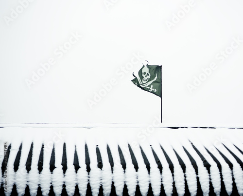 A ragged black pirate flag on a snow-covered roof. photo