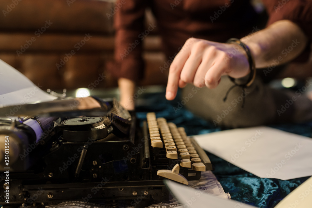 lateral view of man's hand typing on vintage typewriter on a piece of newspaper and dark blue velvet fabric on the floor in a dark room with light bulbs lateral view of man's hand typing on vintage typewriter on a piece of newspaper and dark blue velvet fabric on the floor in a dark room with light bulbs