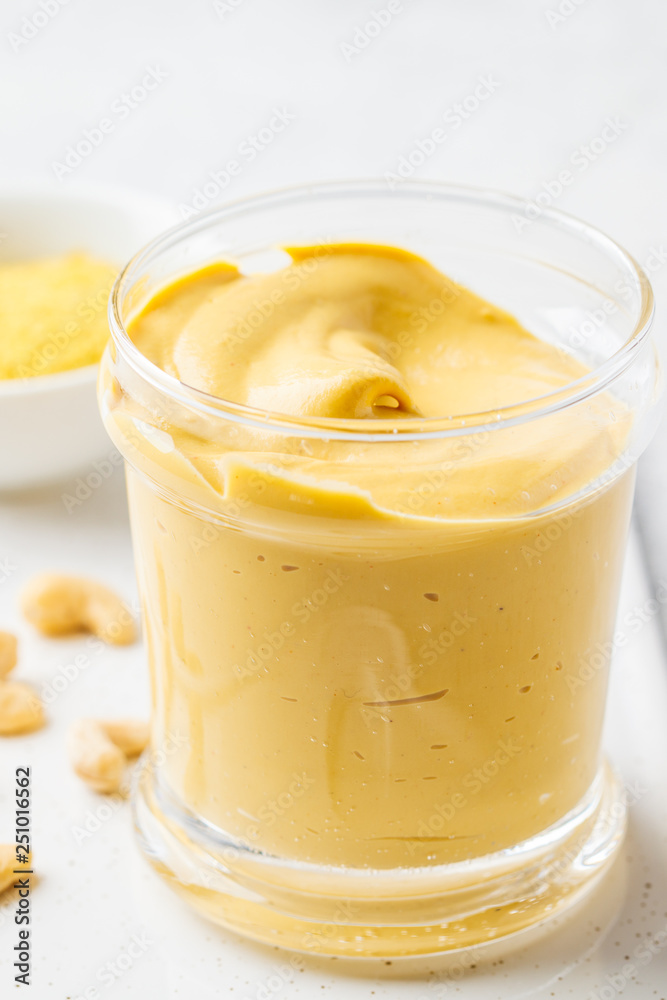 Vegan cashew cheese sauce in a glass, white background.