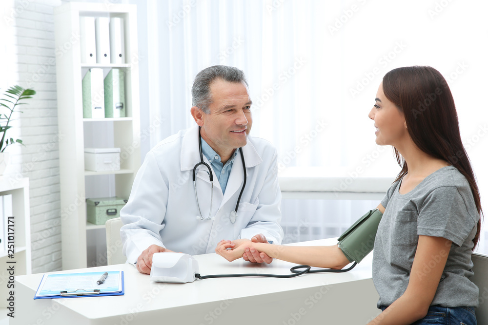 Young woman visiting doctor in hospital. Measuring blood pressure and checking pulse Young woman visiting doctor in hospital. Measuring blood pressure and checking pulse
