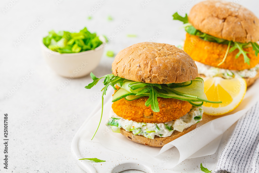 Fish burger with cucumber, arugula and mayonnaise sauce, white background, copy space. Fish burger with cucumber, arugula and mayonnaise sauce, white background, copy space.