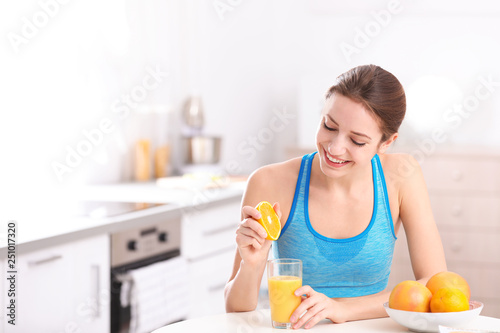 Young woman in fitness clothes making orange juice at home. Space for text