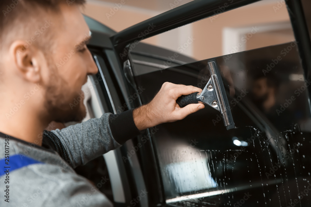 Skilled worker washing car window before tinting in shop Skilled worker washing car window before tinting in shop