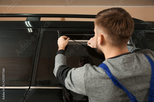 Skilled worker tinting car window in shop