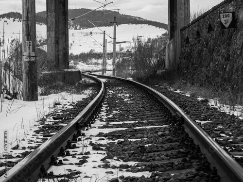 Rail road tracks under a concrete bridge at wintertime in black and white.