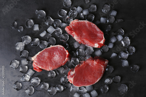 Flat lay composition with raw meat and ice cubes on dark background